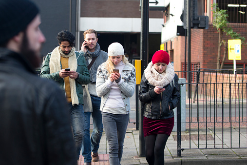 Young people looking at his mobile telephone while crossing a road.