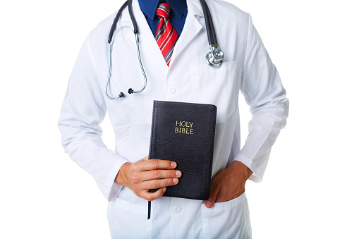 Midsection of male doctor holding Bible against white background