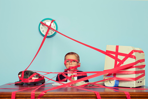 A young boy and businessman is all tied up in rules, regulations and unrealistic expectations. The boy is all taped up with red tape. His business is stuck in red tape and unable to perform. Retro styled.