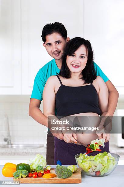 Pregnant Couple Cooking Salad In Kitchen Stock Photo - Download Image Now - 2015, Adult, Asian and Indian Ethnicities