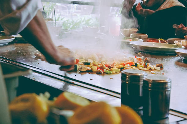 Teppanyaki restaurant: chef cooking in front of guests stock photo