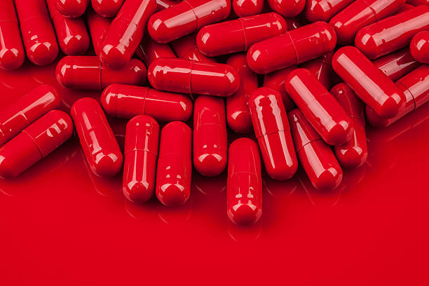 Pila di pillole capsula rossa sulla stessa superficie di colore - foto stock