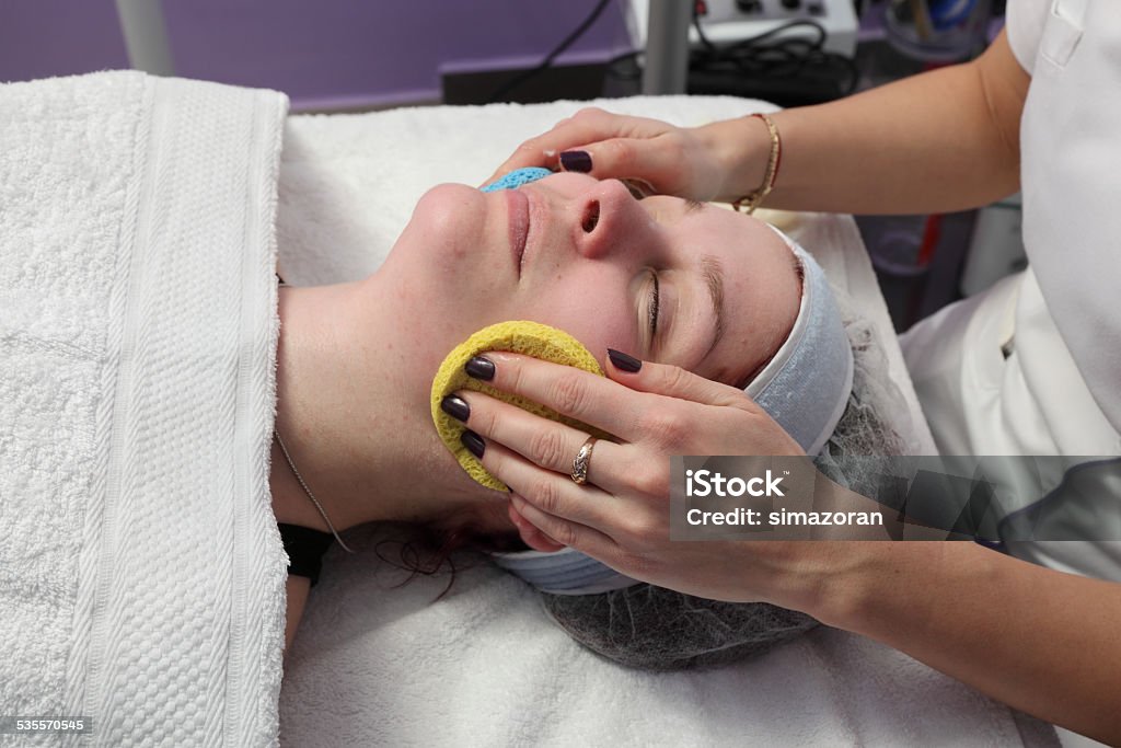 Beauty treatment of young female face Skin treatment, beautician remove cream from face of young female with sponge, real people 2015 Stock Photo