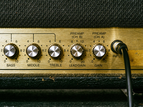 Macro photo of a vintage electric guitar amplifier showing the knobs and input plug..
