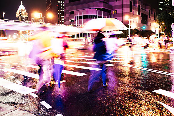 People cross the road holding umbrellas to shelter from the rain, with Taipei 101 visible in the background. Taipei, Taiwan. 
