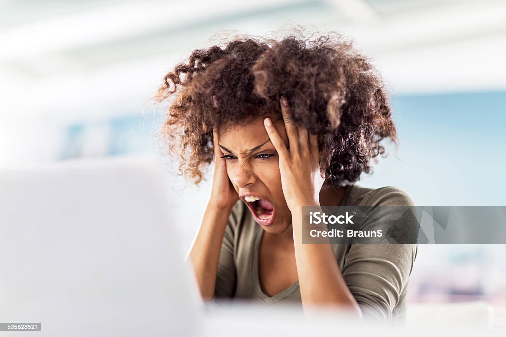 Angry African American woman using computer. Young African American woman using laptop and screaming in despair. She is having some problems. Anger Stock Photo