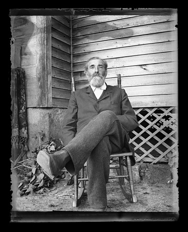 Beautiful Black and White portrait of an American Farmer wearing Victorian-era clothing. Taken on the front porch of his farmhouse dressed in his best clothes--probably on a Sunday afternoon. The image was digitally restored from a glass plate taken circa 1890.