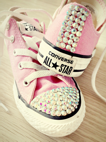 Hertfordshire, UK - February 4, 2015: A pair of girl's pink Converse All Star trainers which have been diamanted on wooden floor.