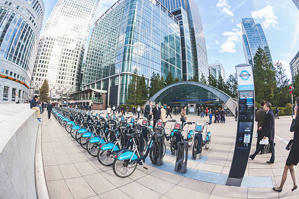 Canary Wharf district with Barclays Cycle Hire docking station London, United Kingdom - October 30, 2013: Canary Wharf district with Barclays Cycle Hire docking station and Underground entrance. Many people, tourists and commuters, are walking in the square. bicycle docking station stock pictures, royalty-free photos & images