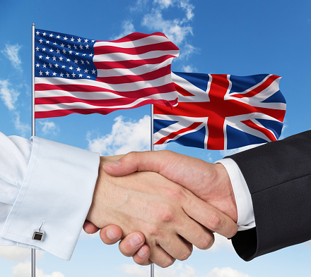 UK and US flags with a handshake on a blue sky background