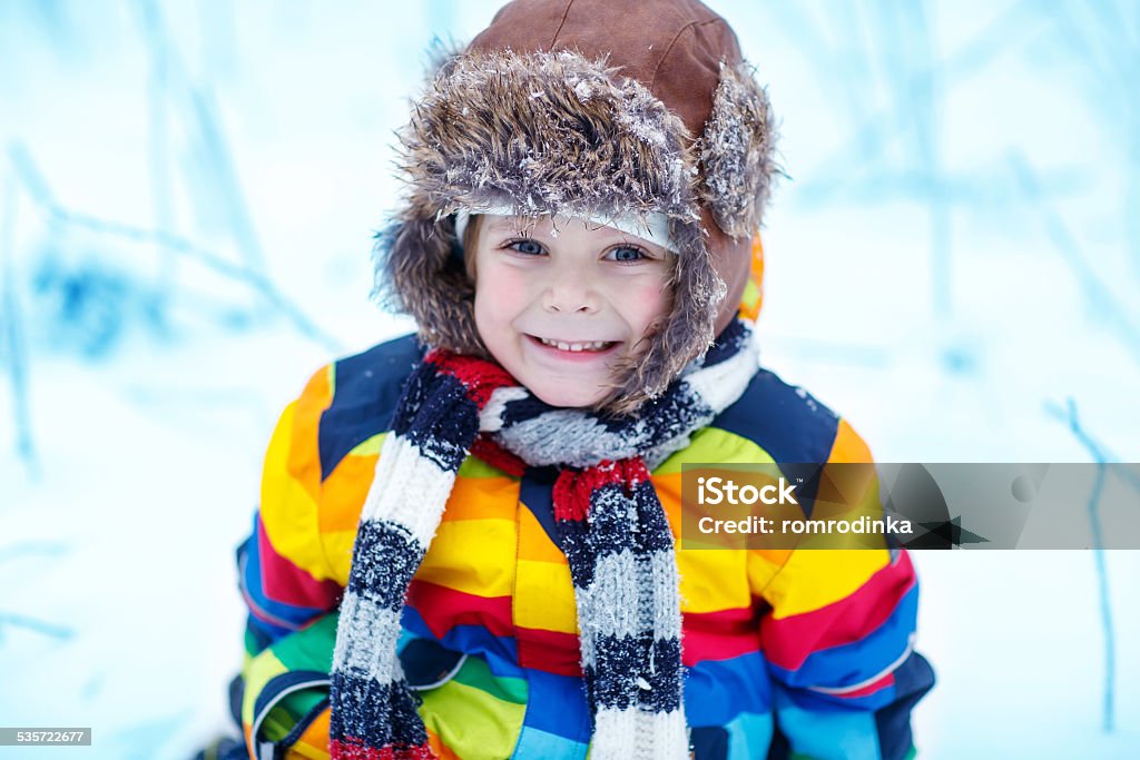 Cute little funny boy in colorful winter clothes having fun Winter portrait of kid boy in colorful winter clothes, outdoors during snowfall. Active outoors leisure with children in winter. Kid with warm hat, hand gloves and scarf 2015 Stock Photo