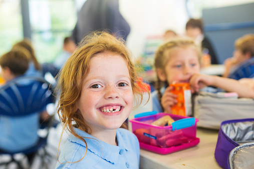 Smiling school students in uniform missing a tooth with a healthy sandwich for lunch