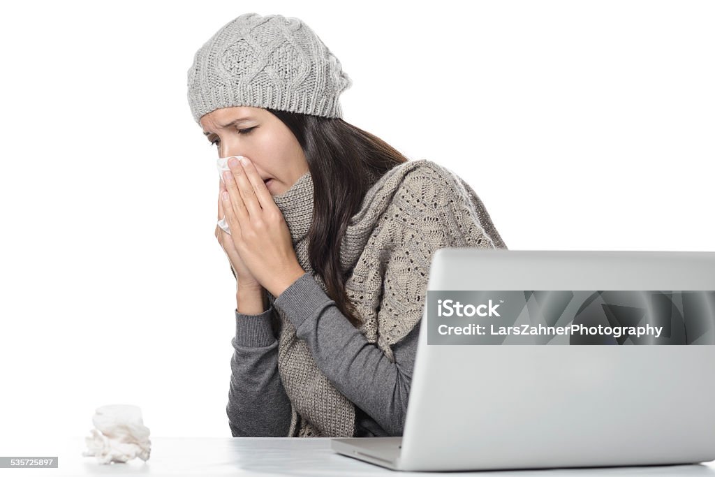 Young businesswoman with a seasonal cold and flu Young businesswoman with a seasonal cold and flu sitting behind her computer blowing her nose on a tissue, isolated on white 2015 Stock Photo