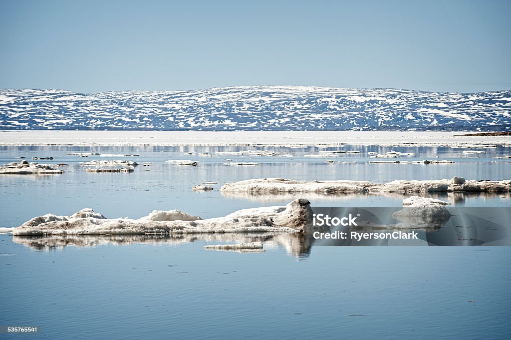 Tundra of Baffin Island, Frobisher Bay, Nunavut, Canada. Tundra of Baffin Island, Frobisher Bay, Nunavut, Canada.  Ice flows float in open water, Blue sky and water, snow on barren rock mountains in background.  Good copy space. 2015 Stock Photo