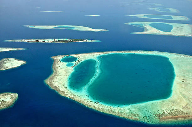 View from waterplane at Maldive island and atoll reef formations Panoramic birds eye view of Maldives North Nilhande Atoll. Shot was taken from a sea plane showing a tiny bounty island with water bungalows surrounded by underwater atoll reef formations with clear blue lagoons, white sandy patches and dark blue canals separating the coral reefs. water bungalow maldives stock pictures, royalty-free photos & images