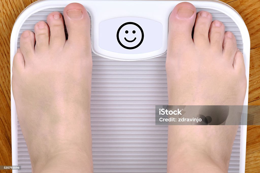 Feet on the scale Barefoot person standing on the weight scale. The scale shows smiley face Above Stock Photo