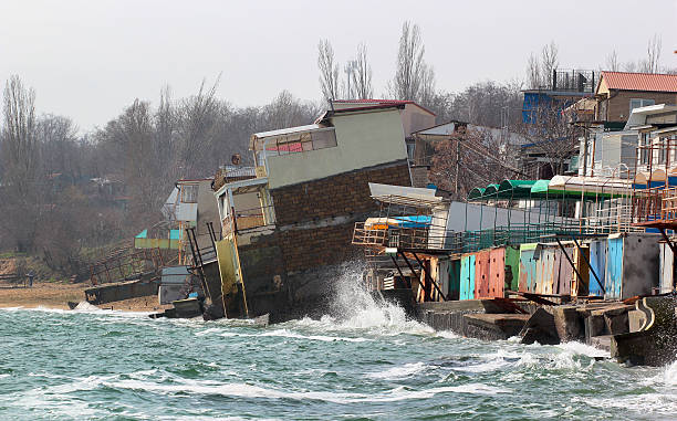 küstenerosion, häuser rutschen ins meer - land in sicht stock-fotos und bilder