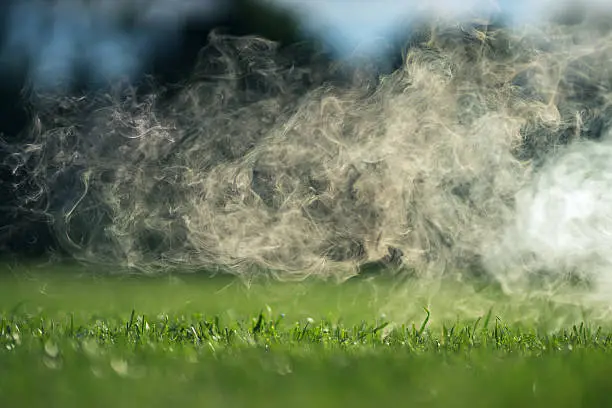 The smoke over the green grass lawn on a Sunny summer day.