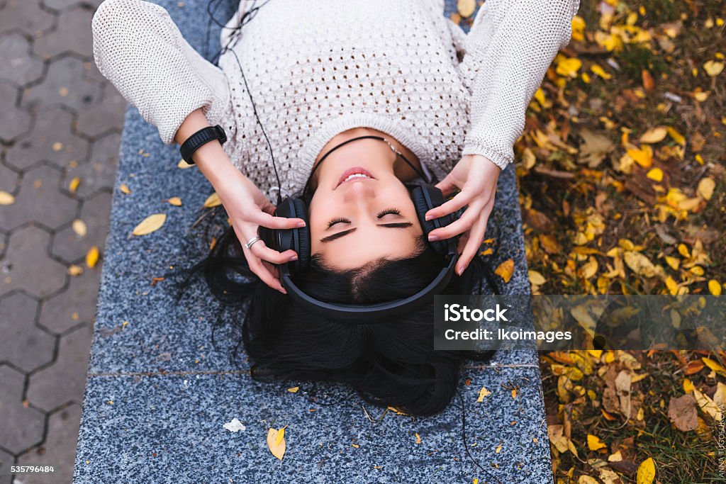 Female student girl outside in park listening to music on Fall life style picture concept. Autumn fallen leaves in park Adult Stock Photo