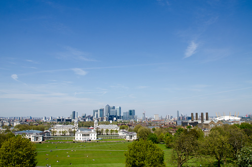 View of Greenwich university Campus from Royal observatory during day in springtime, with skyscrapers of Financial district of London  in background