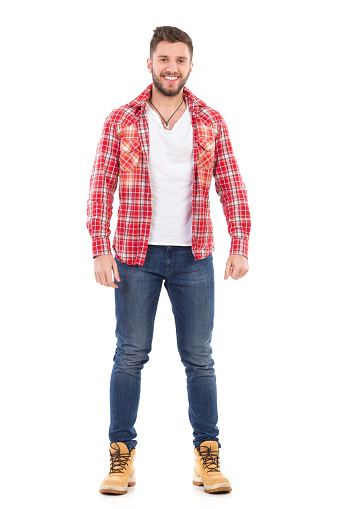 Handsome young man in jeans and lumberjack shirt standing and smiling. Full length studio shot isolated on white.