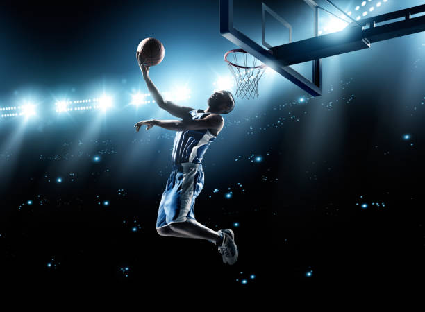 Basketball player in jump shot Close up image of professional basketball player about to do slam dunk during basketball game in floodlight basketball court slam dunk stock pictures, royalty-free photos & images