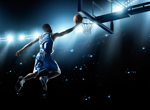 Close up image of professional basketball player about to do slam dunk during basketball game in floodlight basketball court