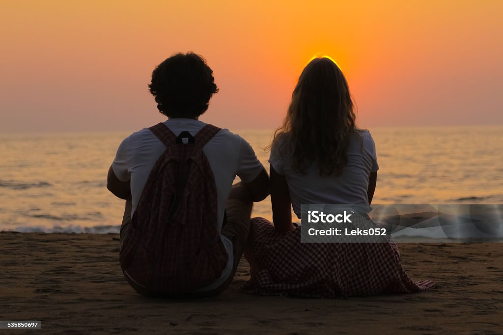 Young Couple is Watching Sunset The young couple on a sea beach is watching the beautiful sunset. 2015 Stock Photo