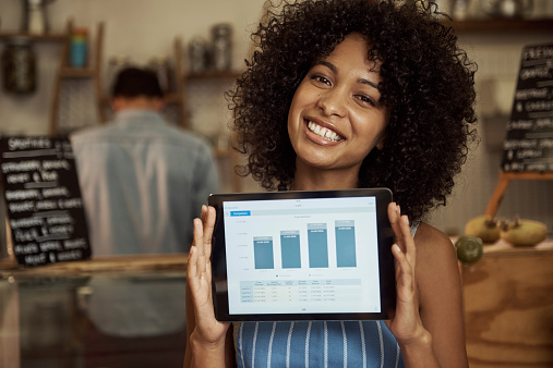 Portrait of a beautiful young woman holding up a digital tablet with a positive growth graph on it