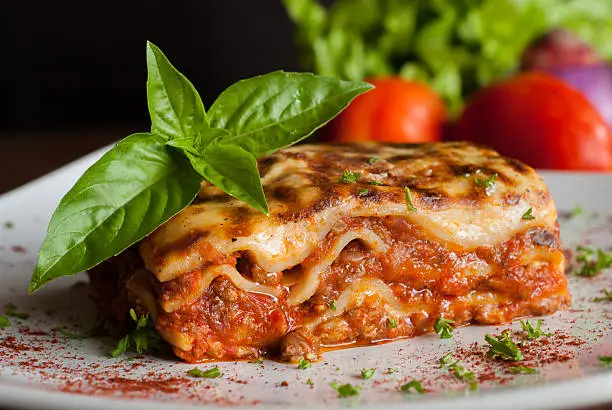 Lasagna on a square white plate with Italian basil