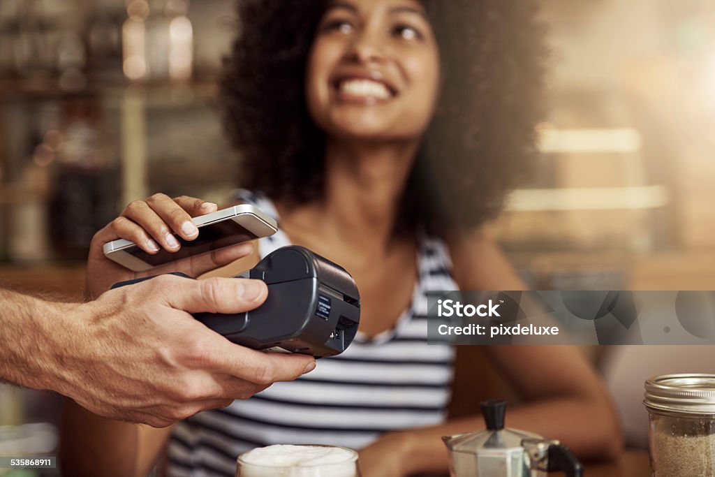 Life's getting easier! Shot of a beautiful woman using her smart phone and an electronic reader to pay her bill in a coffee shop Paying Stock Photo