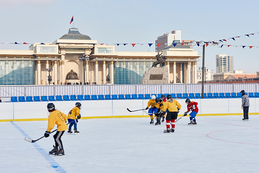 Ulan Bator, Mongolia - January 25, 2015: young mongolians engaged in  a ice hockey match in Chinggis Square. In the background the  Monument to Chinggis Khan.