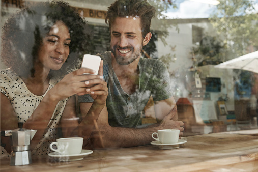 Shot of two friends looking at something on a cellphone, seen through glass