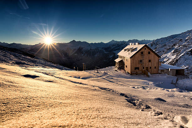 First rays of sun on a mountain hut shinig through the mountain tops