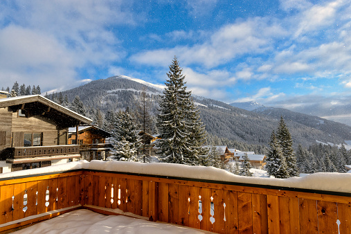 View from the balcony of a chalet in a ski resort in the Austrian Alps during a beautiful winter day. Snow is falling from the sky.