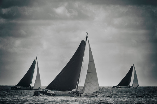 Classic Skutsje sailboats sailing on empty water with a dark sky in black and white. Image with a retro styled vintage look.