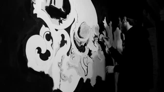 Artist painting white grafiti with skull on the black wall