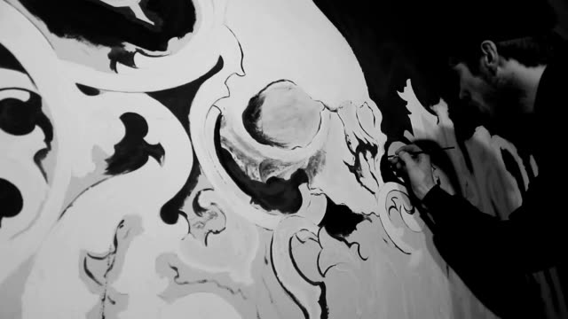 Artist painting white grafiti with skull on the black wall