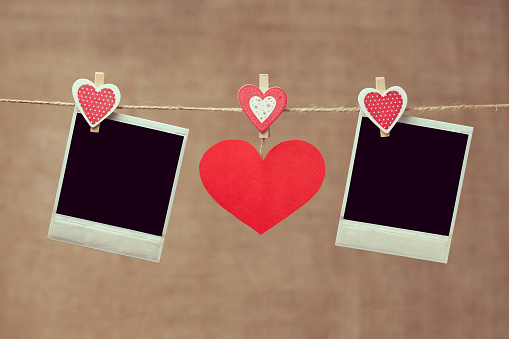 Two polaroid photo frames and red heart for valentines day hanging on vintage background with vintage instagram toning