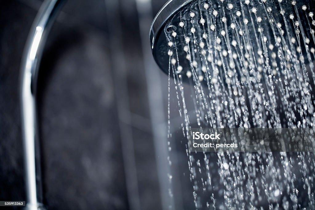 Shower head sprinkling water Close up view of large shower head sprinkling water with black tiles in the background. Shower Stock Photo