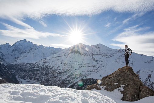 Man stands on summit of snowy peak, looks off, in mountains