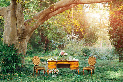 Outdoor composition consisting of two antique chairs and table set for two people and decorated with bouquets of flowers