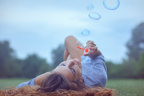 Young woman having fun and blowing bubbles outdoors. Shallow DOF; Soft focused; Developed from RAW; Retouched with special care and attention; Small amount of grain added for best final impression; Ready made for print and web use.