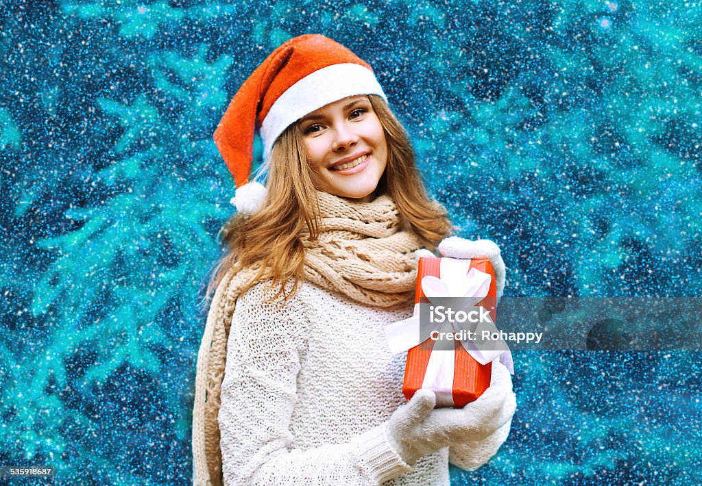 Christmas and people concept - happy pretty woman Christmas and people concept - happy pretty woman in red hat with box gift near christmas tree in winter snowy day 2015 Stock Photo