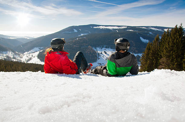 jovem casal feliz deitado em montanhas cobertas de neve. férias de esportes de inverno - chearful - fotografias e filmes do acervo