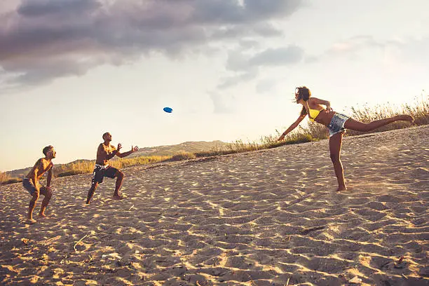 Happy friends playing on the beach with a freesbi .