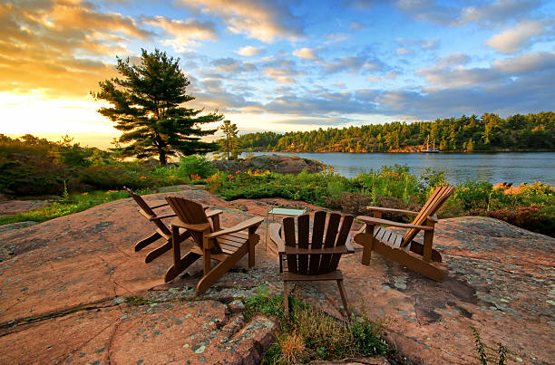 Serene image from cottage living Cottage life begins in the morning, when the rising sun shines on muskoka chairs, sailboat and garden cottage life stock pictures, royalty-free photos & images