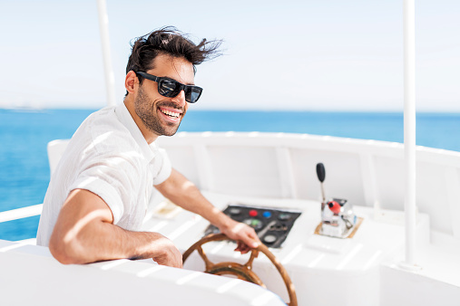 Happy young man driving a boat and turning towards the camera.