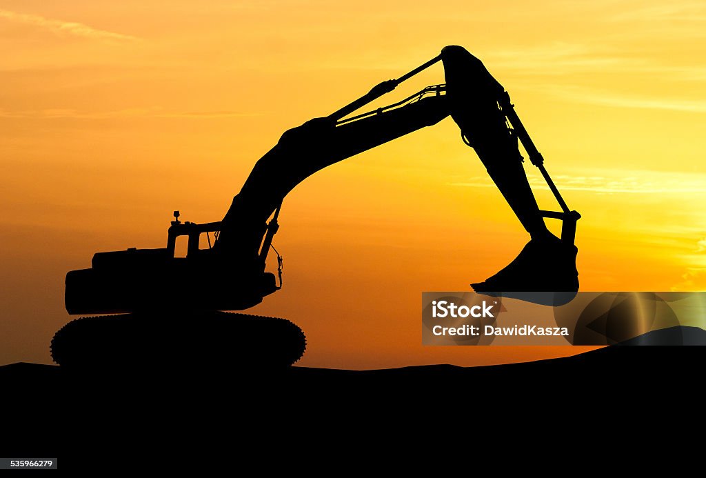 silhouette of Excavator loader at construction site with raised silhouette of Excavator loader at construction site with raised bucket over sunset In Silhouette Stock Photo