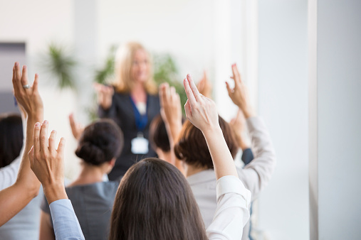 Group of businesswomen attending a seminar, raising their hands. Focus on hands. Unrecognizable people.